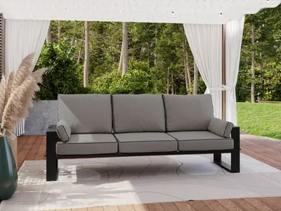 An outdoor sofa on a wooden deck with curtains and trees in the background.