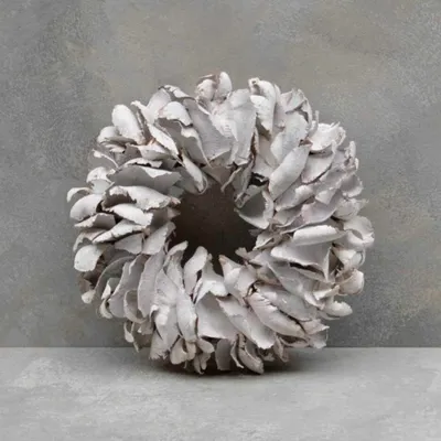 A white palm petal wreath is displayed on a gray surface against a gray textured background.