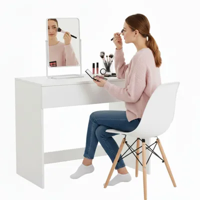 A woman is applying makeup at a white vanity table.