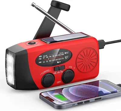 A red and black solar-powered emergency radio with a flashlight and a smartphone connected to it.