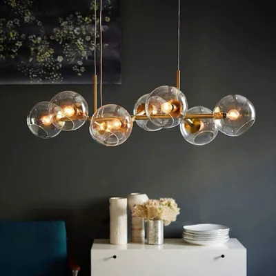 A modern chandelier with glass globes hangs above a white dresser with decorative items.