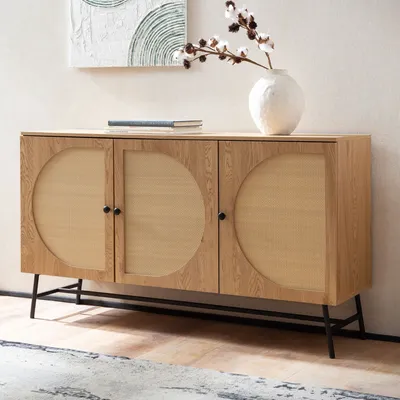 A wooden sideboard with rattan woven doors sits against a wall with artwork above it.