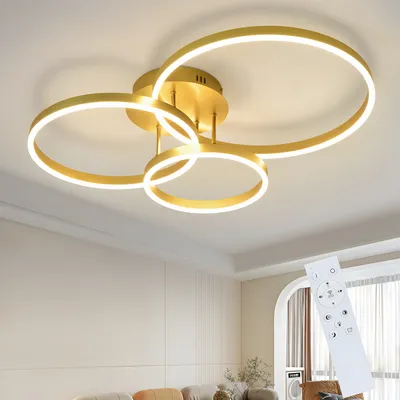 A modern gold ceiling light with three rings and LED lighting, shown installed on a ceiling. A remote control is also visible in the foreground.