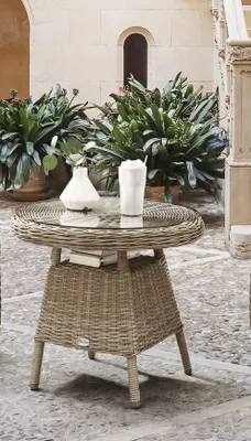 An outdoor patio setting with a wicker table and chairs, surrounded by plants.