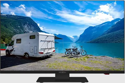 A camper van and two bicycles are parked by a lake with mountains in the background.