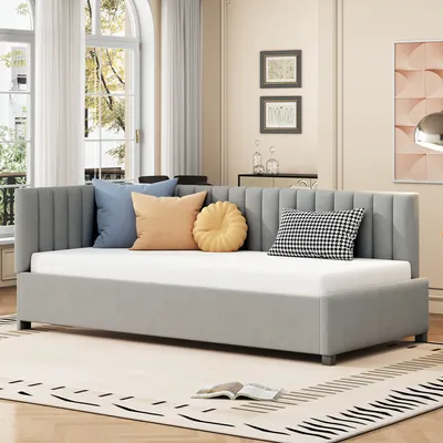 A daybed with several decorative pillows is shown in a well-lit room with large windows and a rug.