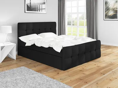 A black boxspring bed with white bedding is shown in a bedroom setting with wooden floors, a grey rug, and a window with curtains in the background.