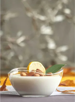 A close-up shot of a dessert in a glass bowl, garnished with almonds, a lemon slice, and a leaf.
