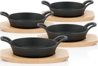 Four cast iron serving pans with wooden bases are arranged in a staggered pattern against a white background.
