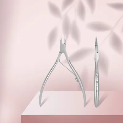 Two cuticle nippers are displayed on a pink surface with a soft leaf shadow effect in the background.