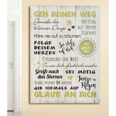 A motivational sign with German text on a wooden background, leaning against a wall.