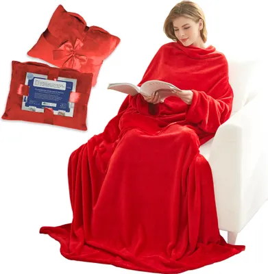 A woman is sitting on a white couch, reading a book while wrapped in a red blanket with sleeves.