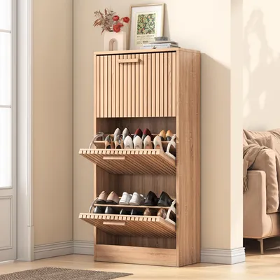 A wooden shoe cabinet with multiple flip-down compartments filled with shoes, placed in a room with a window and a sofa visible in the background.
