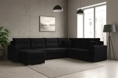 A black sectional sofa with an ottoman is placed in a modern living room with concrete-look walls and a large window.