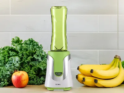 A blender with fruits and vegetables on a countertop.