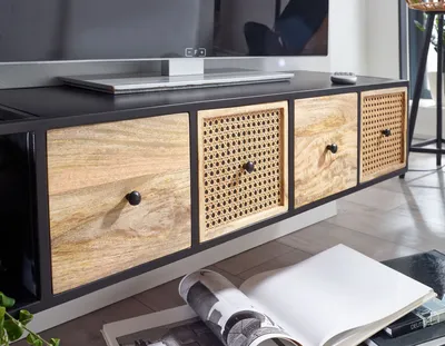 A close-up of a wooden TV stand with multiple drawers and cane-woven inserts, with a TV on top and a magazine on the floor in front.