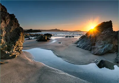Produktbild von Wallario Fototapete Vliestapete, seidenmatte Oberfläche, einfache Verarbeitung, Größe 200 x 140 cm, Motiv Sonnenuntergang hinter einem Felsen am Strand