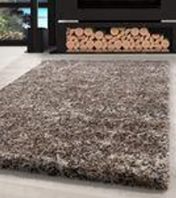 A shaggy rug in front of a fireplace with stacked logs.