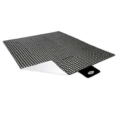 A picnic blanket with a black and white gingham pattern is shown laid out on a white background. A small black pouch with a logo is attached to the corner of the blanket.
