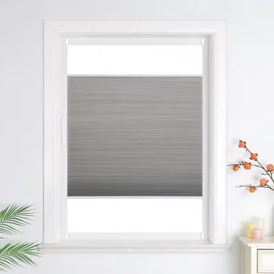 A gray pleated blind is installed in a white window frame.