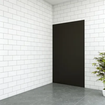 A corner of a room with white tiled walls, a black rectangular panel, and a gray tiled floor. A plant is visible on the right.