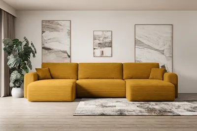 A modern living room with a large, mustard-yellow sectional sofa as the focal point. The sofa is arranged in a U-shape and is placed on a wooden floor with a patterned rug underneath. Two abstract paintings hang on the wall behind the sofa, and a large pot