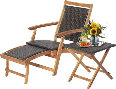 A wooden deckchair with a woven seat and back, accompanied by a small folding side table holding a vase of sunflowers and a bowl of fruit.