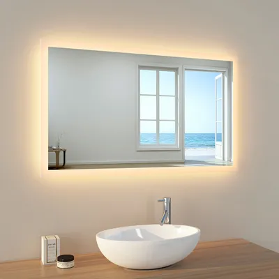 A modern bathroom vanity with a sink and a large illuminated mirror reflecting a bright window overlooking the ocean.