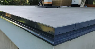 A close-up view of a grey aluminum gutter system on the edge of a flat roof.