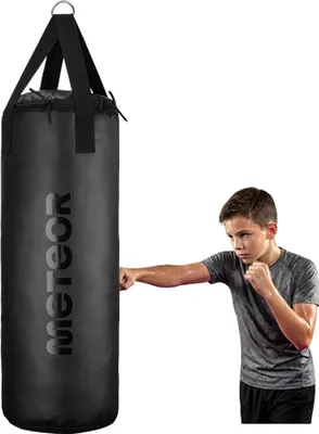 A young boy is punching a black punching bag.