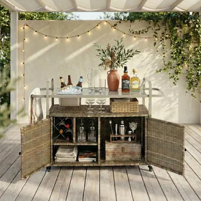 An outdoor patio bar cart set up for serving drinks, with string lights overhead and greenery.