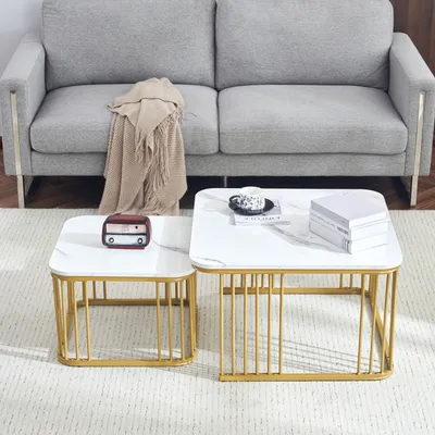 Two square coffee tables with white marble tops and gold metal frames are placed on a rug in front of a gray sofa.