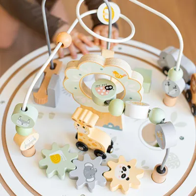 A close-up of a wooden activity table for children, with a child's hands interacting with the toy.
