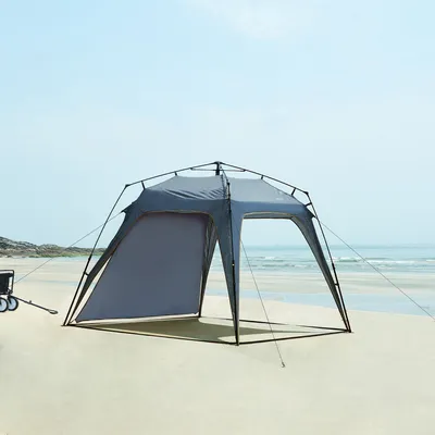 A gray beach tent is set up on a sandy beach with the ocean and sky in the background.