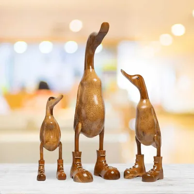 Three wooden duck figurines with boots stand on a white surface against a blurred background.