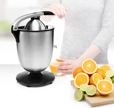 A person using a stainless steel electric citrus juicer with oranges and limes on a counter.