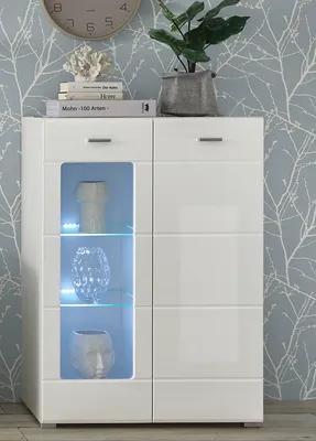 A white highboard cabinet with glass doors and internal lighting, displaying decorative vases. A clock and a plant are on top of the cabinet.