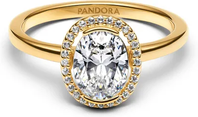 A close-up studio shot of a gold Pandora ring with a large oval diamond and a halo of smaller diamonds.