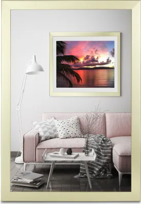 A living room scene with a pink sofa, a floor lamp, and a framed picture of a sunset over the ocean.