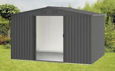 A dark gray metal shed with double doors is shown in a grassy yard with trees and bushes in the background.