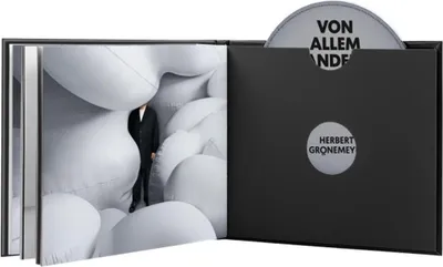 An open book-style case with a CD and a book inside. The book has a person in a suit standing among white inflatable shapes.