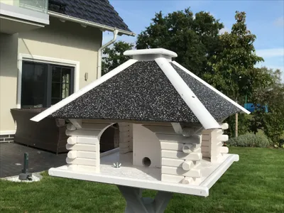 A birdhouse on a stand in a garden, with a house in the background.