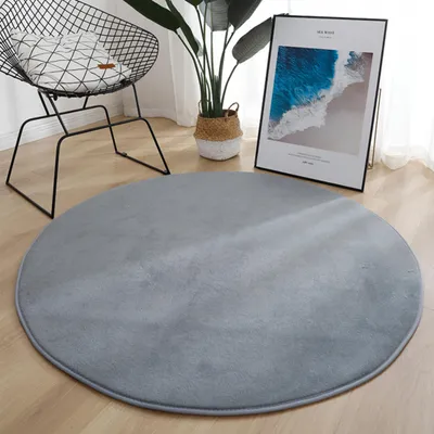 A round gray rug is placed on a wooden floor in a room with a chair, a plant, and a framed picture.