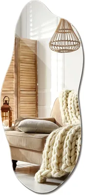 A mirror reflecting a cozy living room scene with a chair, blanket, and lamp.