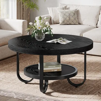 A round, black coffee table with a lower shelf is placed in a living room setting, next to a sofa.