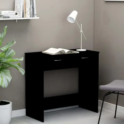 A black desk with a book and a lamp on it, placed in a room with a plant and a chair.
