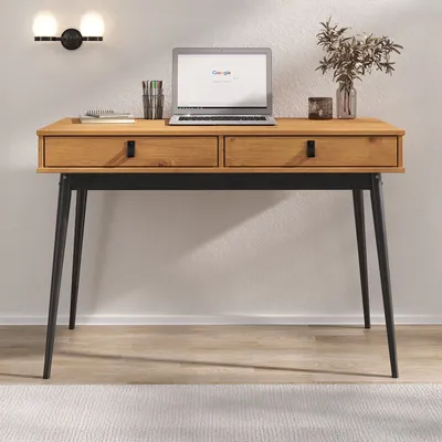 A wooden desk with black metal legs, a laptop, and decorative items on a light-colored floor and white wall.