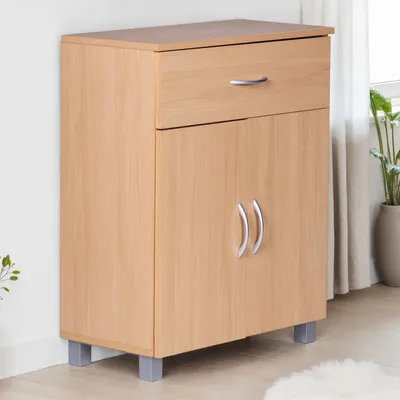 A light brown wooden sideboard with a drawer and two doors, standing on gray legs, against a white wall and next to a window with curtains and a plant.