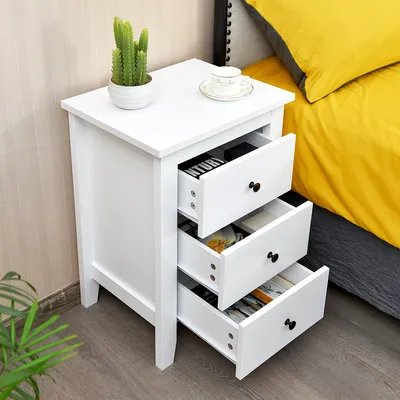 A white nightstand next to a bed with yellow bedding.