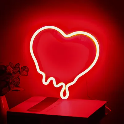 A red neon heart light with dripping effect, placed on a red surface.